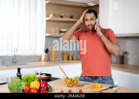 Triste et confus, un jeune homme afro-américain en t-shirt rouge tient la tête avec des appels au téléphone, a eu de mauvaises nouvelles inquiétantes Banque D'Images