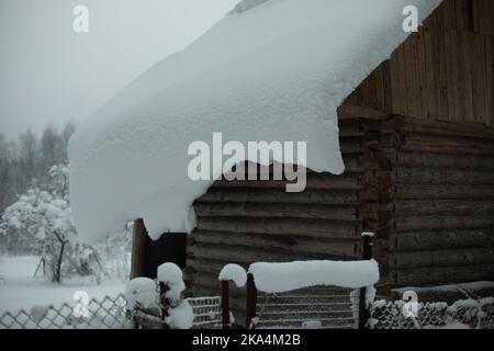 Maison dans village en hiver. Il y a beaucoup de neige sur le toit de la vieille maison. Vue sur le village en forêt. Banque D'Images