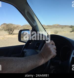 Gros plan de la main d'un homme sur un volant en conduite dans un paysage désertique, Oman Banque D'Images