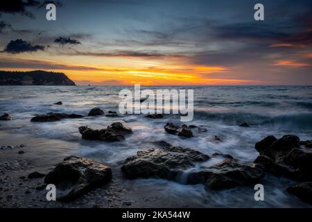 Un paysage marin de longue exposition de vagues se lavant sur des rochers sur la plage au coucher du soleil. Banque D'Images