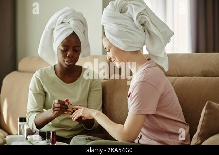 Portrait de deux filles avec des serviettes de toilette faisant la manucure à la maison tout en appréciant la journée de soin de soi ensemble Banque D'Images