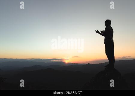 Homme priant au coucher du soleil montagnes, concept vacances en plein air harmonie avec la nature paysage, Voyage style de vie détente spirituelle méditant émotif. Banque D'Images