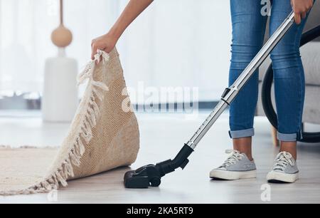 Aspirateur, sol et femme nettoyant sous un tapis dans le salon d'une maison. Le ménage, le service et le nettoyage passent l'aspirateur dans le salon avec un tapis ou Banque D'Images