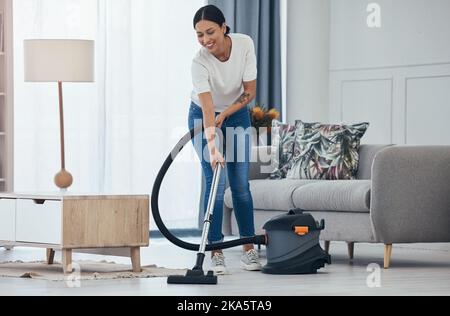 Aspirateur femme noire, sourire dans la salle de séjour et nettoyer le sol des carreaux à la maison pour l'hygiène. Femme de ménage, contente de l'appareil pour le ménage Banque D'Images