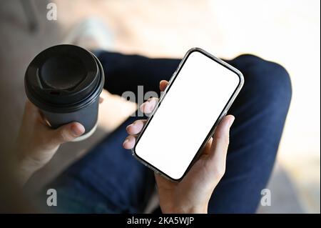 Vue de dessus, Un homme tenant une tasse de café et son smartphone tout en se relaxant dans un café. Téléphone mobile écran blanc maquette Banque D'Images