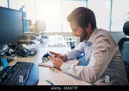 Quelqu'un a un message. Un jeune homme d'affaires focalisé envoie un SMS sur son téléphone portable tout en étant assis derrière son bureau dans le bureau. Banque D'Images