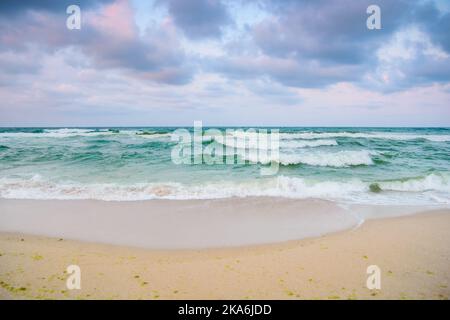 plage de sable avant la tempête. paysage nocturne avec de lourds nuages dans une lumière colorée. vagues turquoise qui se précipitent sur la côte. temps venteux Banque D'Images