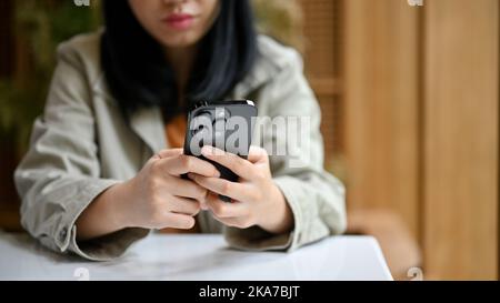 Une jeune femme asiatique fatiguée et contrariée regarde l'écran de son téléphone, attend un appel ou des messages de quelqu'un assis à son bureau. Image rognée Banque D'Images