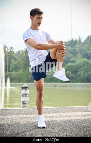 Portrait, Active et beau sportif asiatique dans des chaussures de sport et de course à pied qui étirent sa jambe, réchauffez-vous avant l'entraînement. Banque D'Images