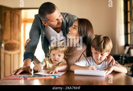 L'image d'une parentalité parfaite. Une jeune famille de quatre personnes qui dessine et qui fait preuve de créativité à la maison. Banque D'Images