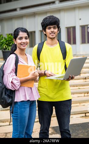 Photo verticale d'étudiants souriants heureux avec sac à dos tenant un ordinateur portable regardant camea à l'université campus - concept de technologie, amitié et compétence Banque D'Images