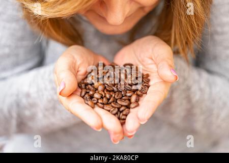 Femme tenant des grains de café dans ses mains tout en sentant l'arôme intense du café. Banque D'Images