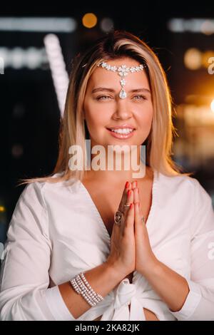 Portrait d'une fille souriante dans une robe blanche avec ses paumes clastées devant elle. Banque D'Images