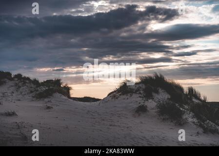 Un immense paysage de nuages sur des dunes de sable herbacées pendant le coucher du soleil Banque D'Images