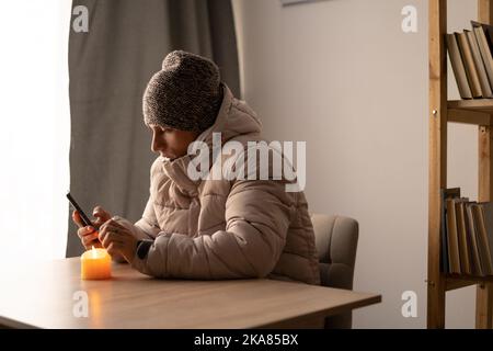 Un jeune malade se sent froid en portant des vêtements chauds en regardant un film sur son smartphone, un gars agacé se dégèle en se réchauffant à la maison enveloppé de tissu écossais, problème Banque D'Images
