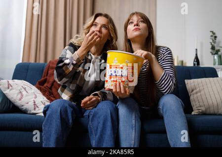 Deux femmes de différents âges mangeant du pop-corn sont concentrées sur regarder un film ou une émission de télévision intéressant Banque D'Images