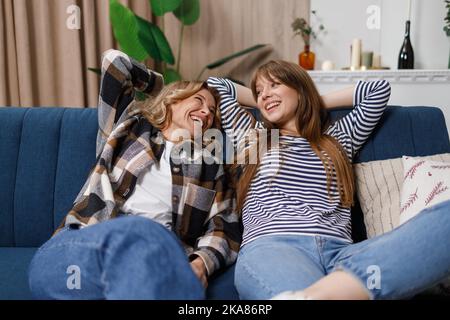 Mère et fille paresseuses sont couchés sur le canapé avec leurs mains au-dessus de leur tête. Deux femmes d'âges différents qui rient se détendent sur le canapé Banque D'Images