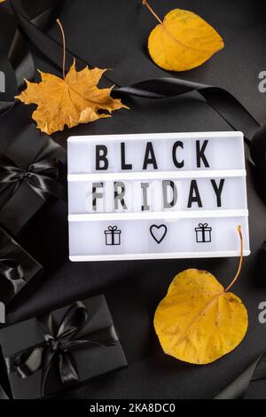 Disposition à plat de boîtes enveloppées de noir, boîte lumineuse avec lettres Vendredi noir, feuilles d'automne jaunes sur fond noir. Grande conce de vente du Vendredi fou Banque D'Images