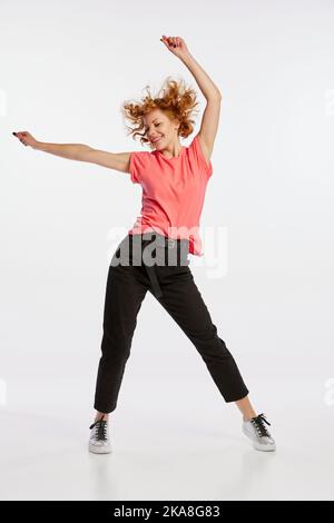 Excitée belle jeune femme à tête rouge dansant isolée sur fond blanc studio. Émotions humaines, expression faciale, concept de beauté. Banque D'Images