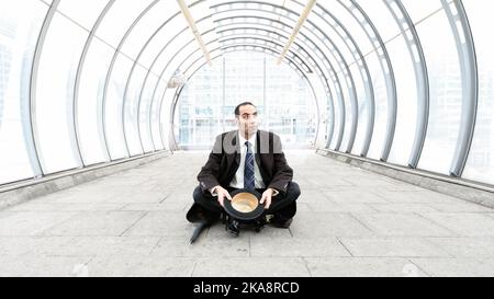 Le City Gent, Cap en main. Un homme d'affaires londonien traditionnel utilisant son chapeau de melon mendiant dans un environnement urbain moderne. À partir d'une série d'images associée. Banque D'Images