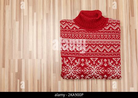 Pull de Noël tricoté rouge à col roulé de conception traditionnelle avec ornement géométrique scandinave blanc (alias Ugly Sweater) posé plié sur une bette en bois Banque D'Images