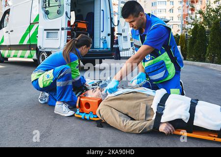 Ambulanciers paramédicaux avec défibrillateur effectuant une réanimation cardiopulmonaire sur un patient cardiaque allongé sur un brancard d'urgence Banque D'Images