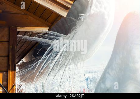 Vue détaillée de la fonte des glaces sur le toit de cabane alpine en bois, dans une montagne venteuse. De grandes glaces à croquer sur un hiver froid et ensoleillé Banque D'Images