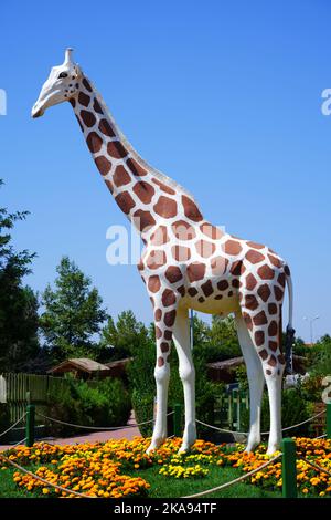 Statue de girafe en plastique au parc avec des fleurs colorées en plein air Banque D'Images