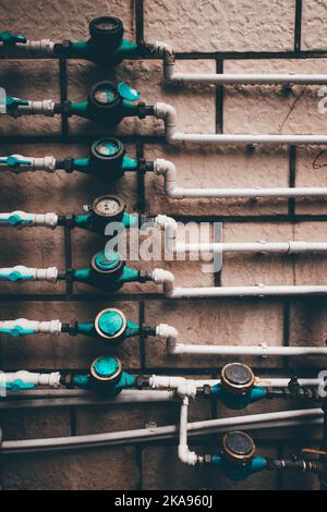 Un cliché vertical de compteurs d'eau résidentiels et de tuyaux sur fond de mur en pierre Banque D'Images