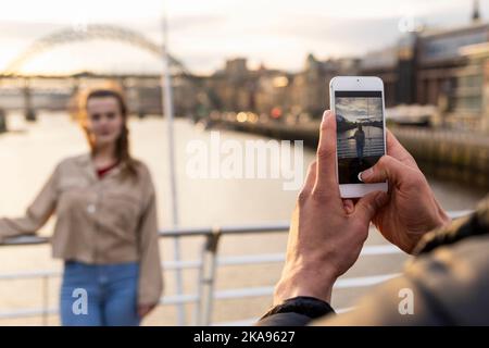 Un jeune couple passe la journée à Newcastle upon Tyne. La femme pose pour une photo que son petit ami prend sur un téléphone portable alors qu'elle est debout Banque D'Images