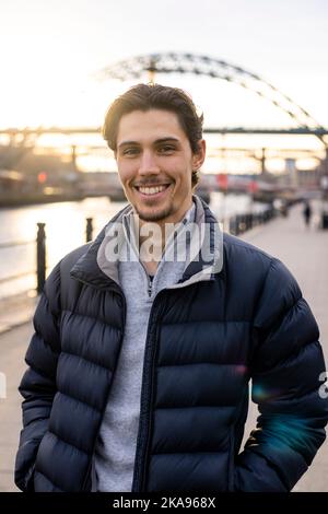 Un jeune homme passant la journée à Newcastle upon Tyne. Il est debout sur un chemin à côté de la rivière Tyne tout en regardant la caméra et en souriant avec lui Banque D'Images