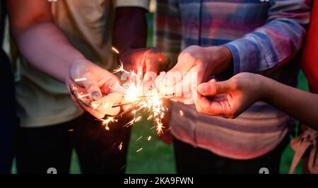 Des amis heureux qui fêtent et applaudissent avec des escroers la veille du nouvel an - se concentrer sur la main droite tenant feu d'artifice Banque D'Images