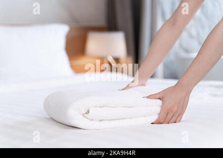 Un gros plan de mains mettant pile d'une serviette de bain blanche fraîche sur la drap de lit Banque D'Images