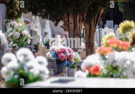 Foyer sélectif d'un bouquet de fleurs en plastique sur une tombe de cimetière, hors foyer autour de bouquets colorés de fleurs naturelles, Toussaint Day, Novembe Banque D'Images