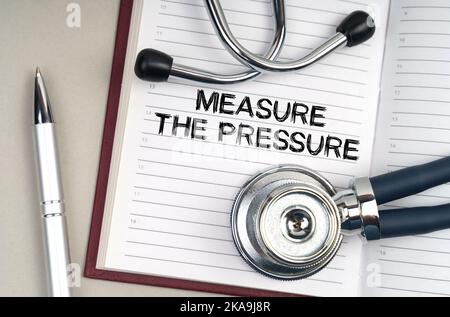 Concept de médecine. Sur la table se trouve un stéthoscope, un stylo et un bloc-notes dans lequel il est écrit - mesurer la pression Banque D'Images