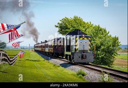 Strasburg, Pennsylvanie. 48 juin 2021 - vue de Thomas le train tirant des voitures de tourisme tout en passant les drapeaux américains sur une clôture le jour du soleil Banque D'Images