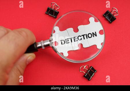 Concept d'entreprise. Un homme regarde à travers une loupe aux puzzles avec l'inscription - DÉTECTION Banque D'Images