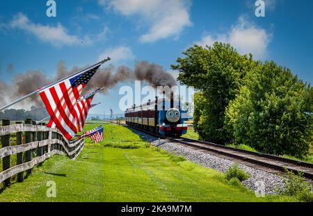 Strasburg, Pennsylvanie. 48 juin 2021 - vue de Thomas le train tirant des voitures de tourisme tout en passant les drapeaux américains sur une clôture le jour du soleil Banque D'Images