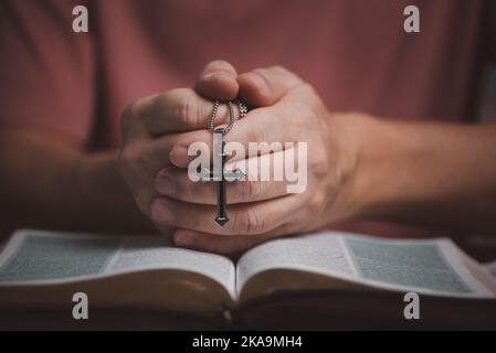 Ouvrez le livre de la Bible sainte avec les mains des gens pliant et tenant le collier de croix dans le livre du milieu priez à Dieu. Banque D'Images