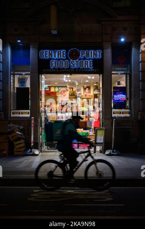 LONDRES - 3 novembre 2020 : entrée de nuit au magasin d'alimentation de Center point avec mouvement silhouette floue du cycliste de livraison en passant devant Banque D'Images