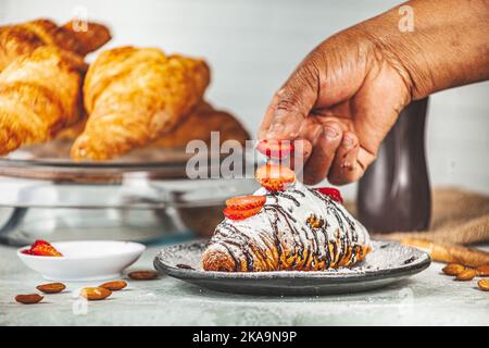 Une personne mettant des fraises tranchées sur un croissant fraîchement cuit avec de la poudre de sucre et du chocolat Banque D'Images