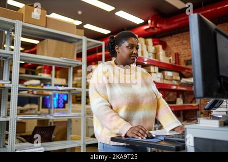 Portrait de la taille de la femme noire adulte utilisant un ordinateur lors de la configuration de machines d'impression dans un magasin industriel, espace de copie Banque D'Images