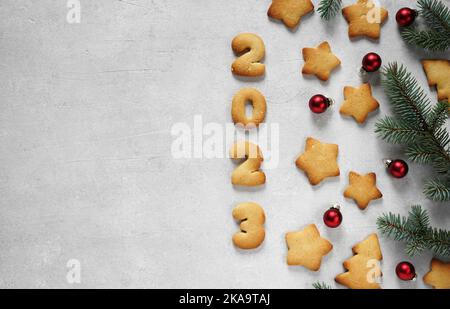 Biscuits sous forme de numéros 2023 sur fond de béton avec brindilles et jouets. Concept nouvelle année, vue de dessus, espace de copie Banque D'Images