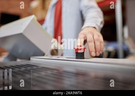 Gros plan d'un jeune homme appuyant sur le bouton rouge de la presse d'impression dans l'atelier industriel, espace de copie Banque D'Images