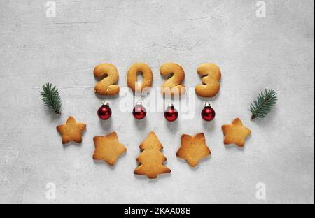 Biscuits sous forme de numéros 2023 au centre sur fond de béton décoré de brindilles de pin et de jouets de noël. Concept nouvelle année, vue du dessus Banque D'Images