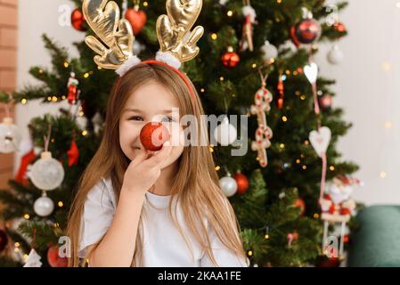 Portrait d'une petite fille mignonne portant des cornes de Rudolf tenant un ballon de fête à son nez. L'enfant dépeint un cerf de Noël Banque D'Images