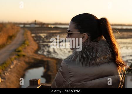 Vue arrière d'une jeune femme caucasienne avec une queue de cheval portant un manteau doré et des lunettes de soleil entre les champs agricoles. Concept de style de vie Banque D'Images
