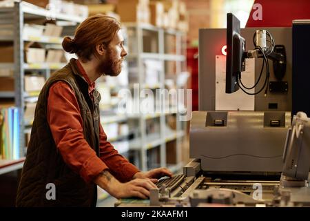 Vue latérale d'un homme travaillant avec une machine d'impression à l'usine d'impression Banque D'Images