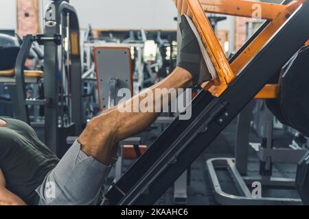 Presse de jambe de gym professionnelle utilisée par une personne caucasienne méconnaissable en short gris. Processus de construction des muscles du corps. Jour de la jambe. Photo de haute qualité Banque D'Images