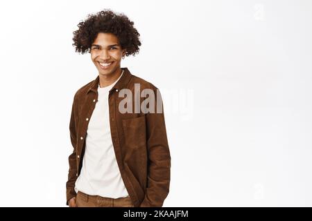 Portrait d'un homme hispanique souriant au visage confiant, tenant les mains dans les poches, debout à la légère sur fond blanc Banque D'Images